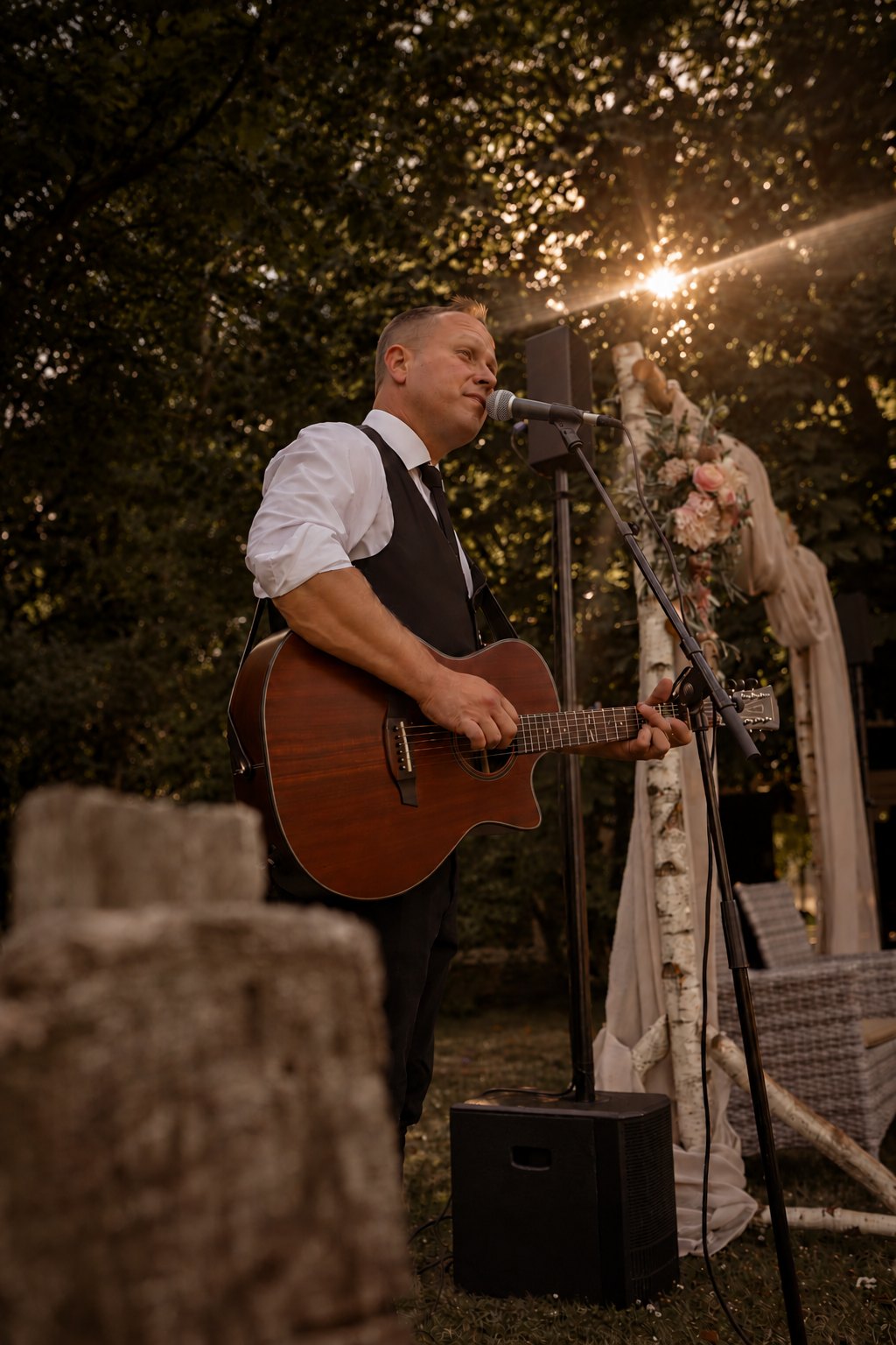 John Eid singt und spielt Gitarre bei einer Hochzeit, Sonnenstrahlen im Hintergrund